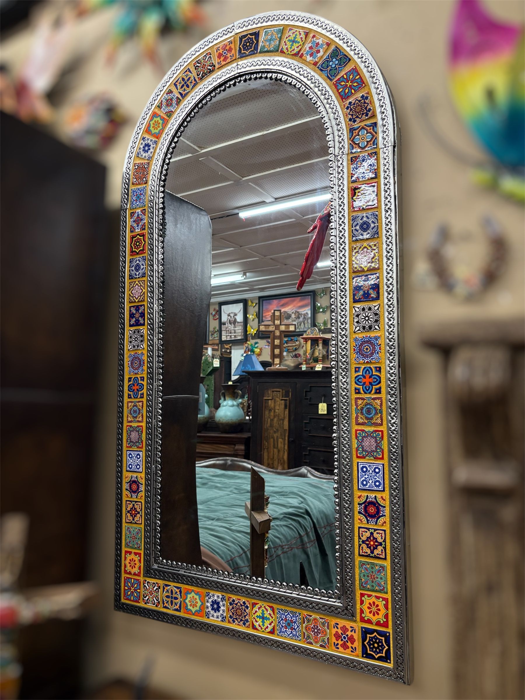 Arched mirror with a tiled border and a silver frame, reflecting a room with furniture.