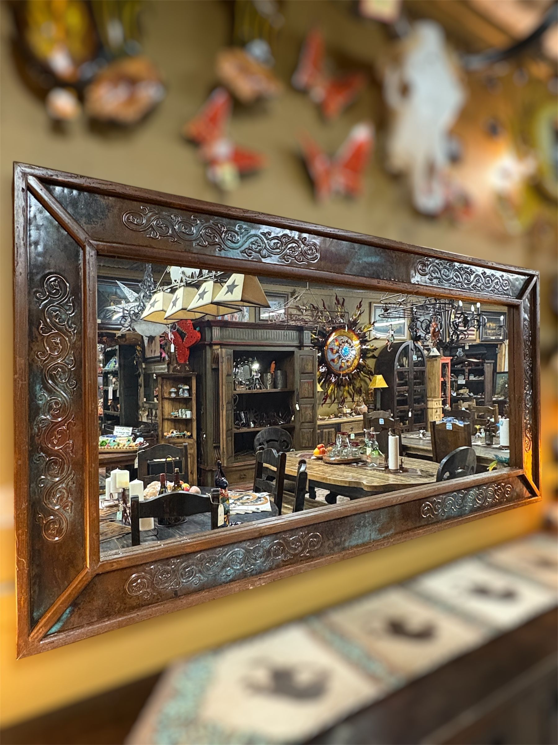 Rectangular mirror with a decorative brown frame, reflecting a cluttered shop filled with antiques and curios.