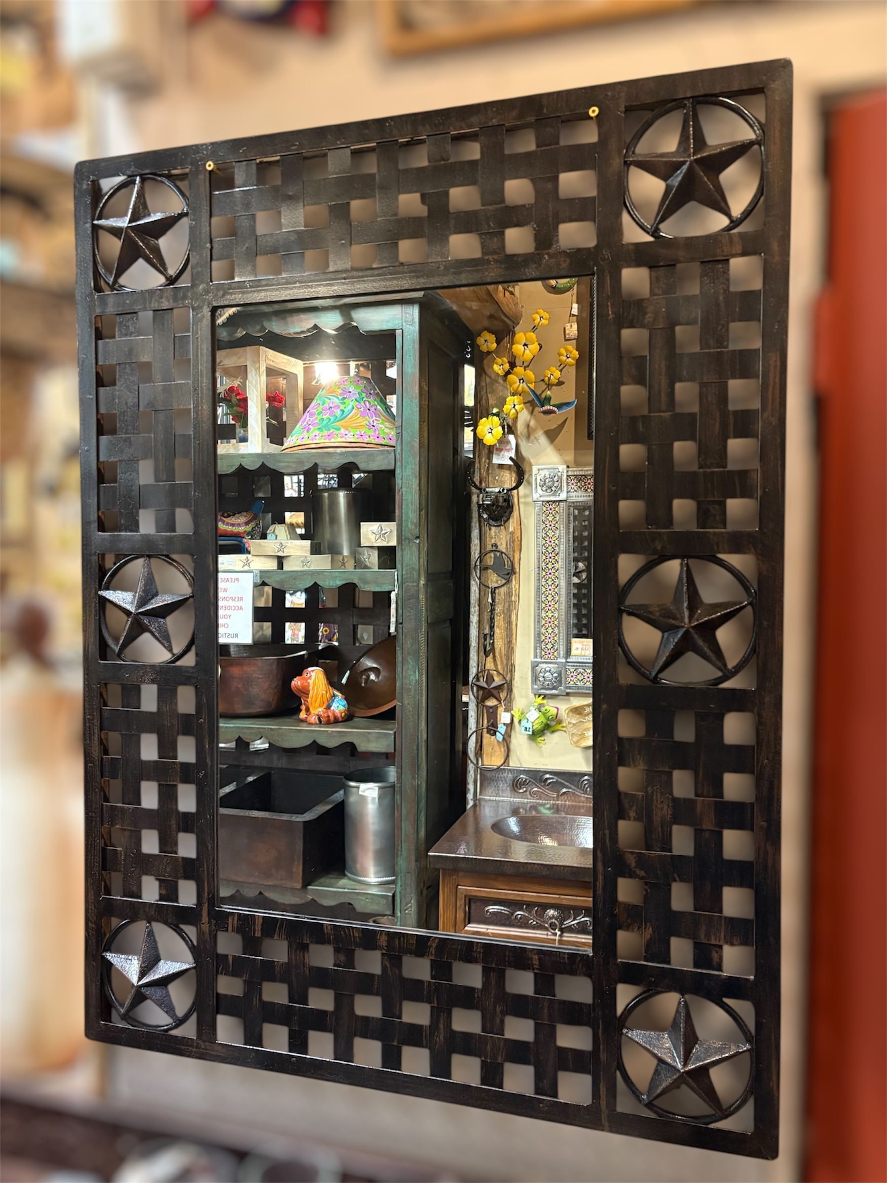 A rectangular mirror with a dark, woven metal frame and star accents. The mirror reflects a store interior.