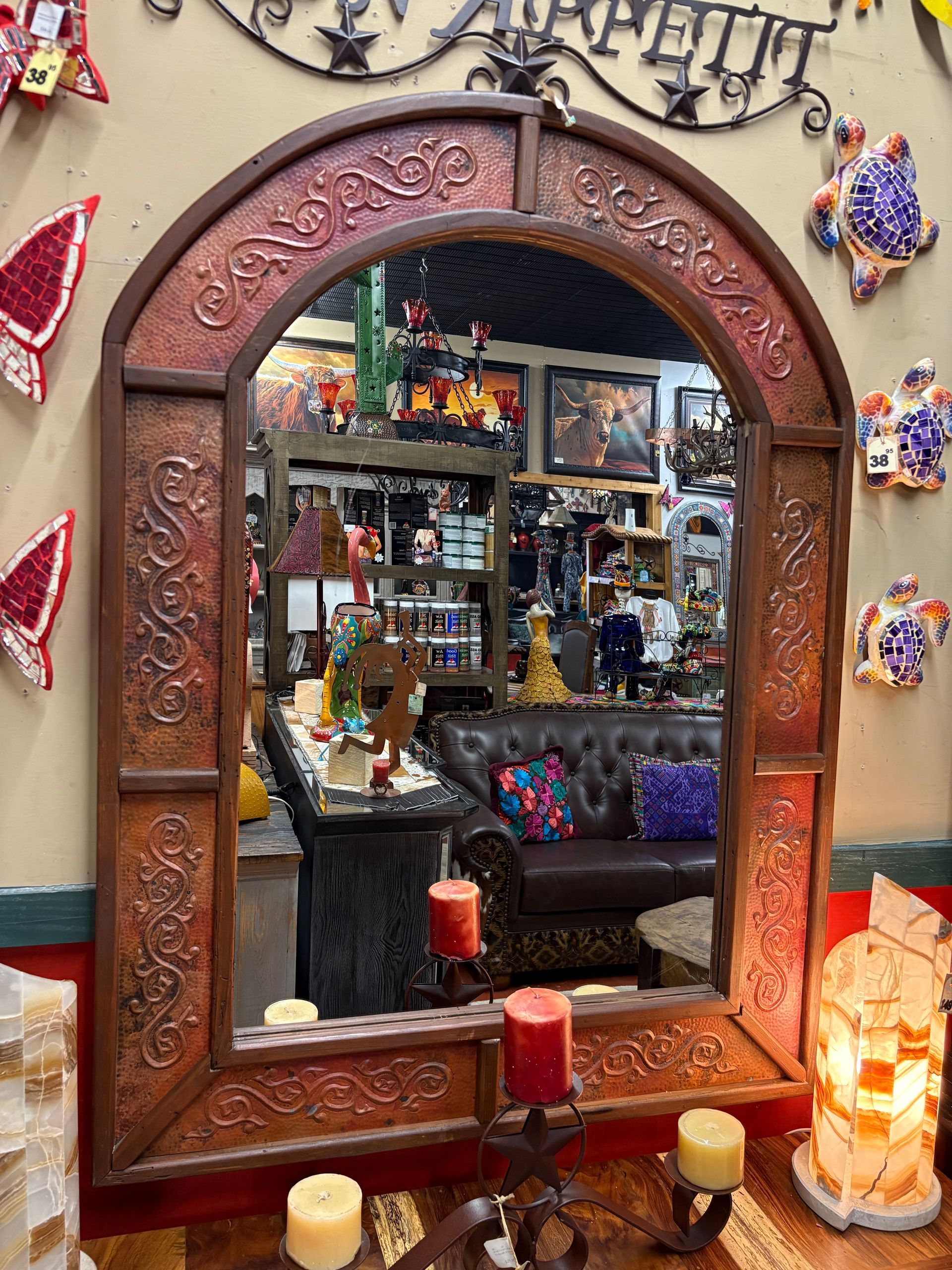 Arched, copper-framed mirror reflecting a shop's interior; shelves with merchandise and a seating area.