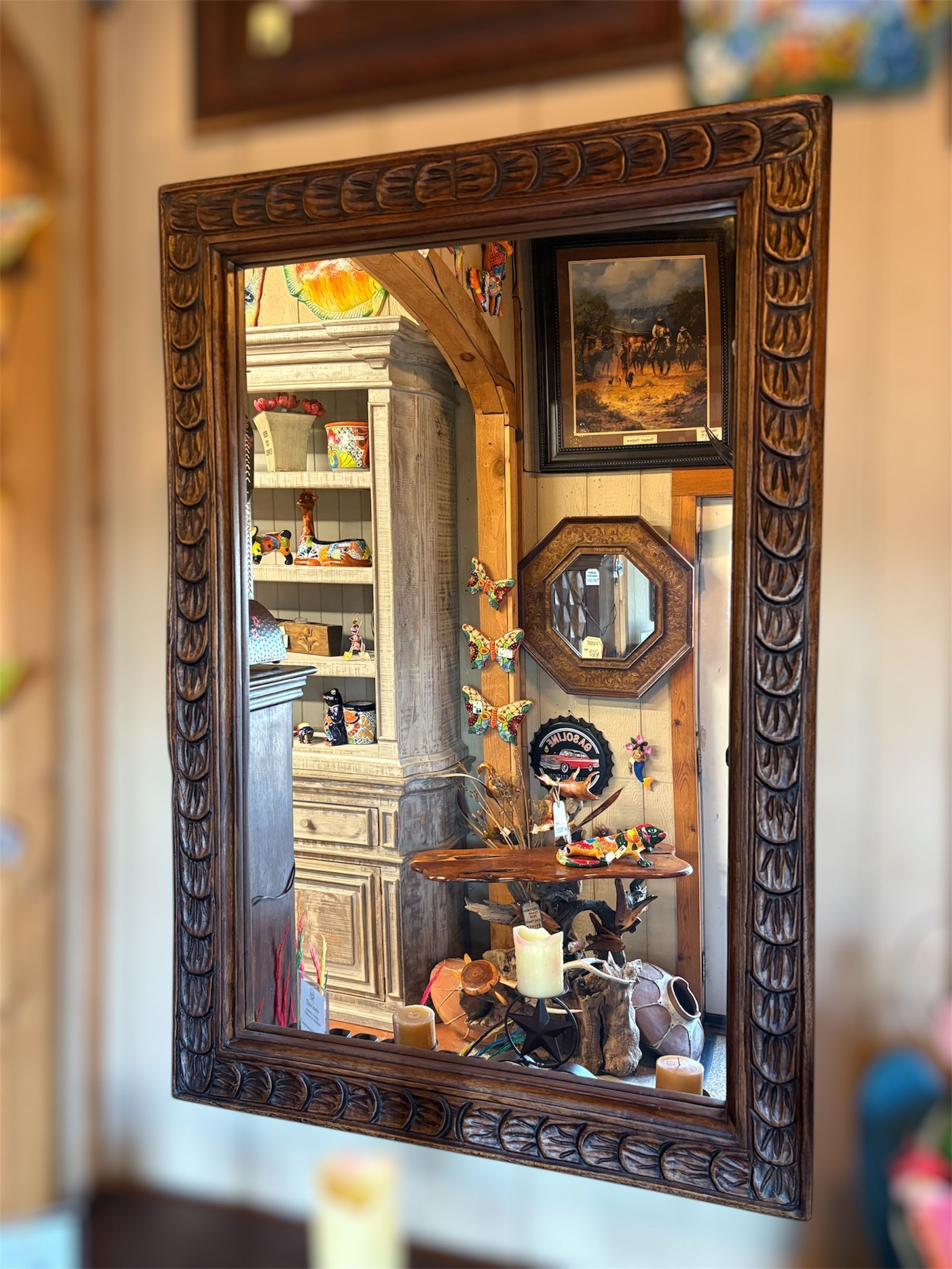 Large ornate brown mirror reflects a cluttered room with various objects, including a cabinet, paintings, and decorations.