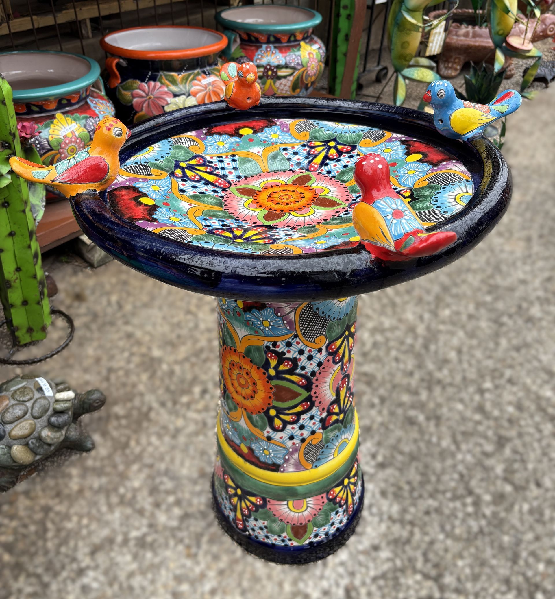 A colorful, ceramic birdbath with a patterned bowl and pedestal, decorated with small bird figurines.
