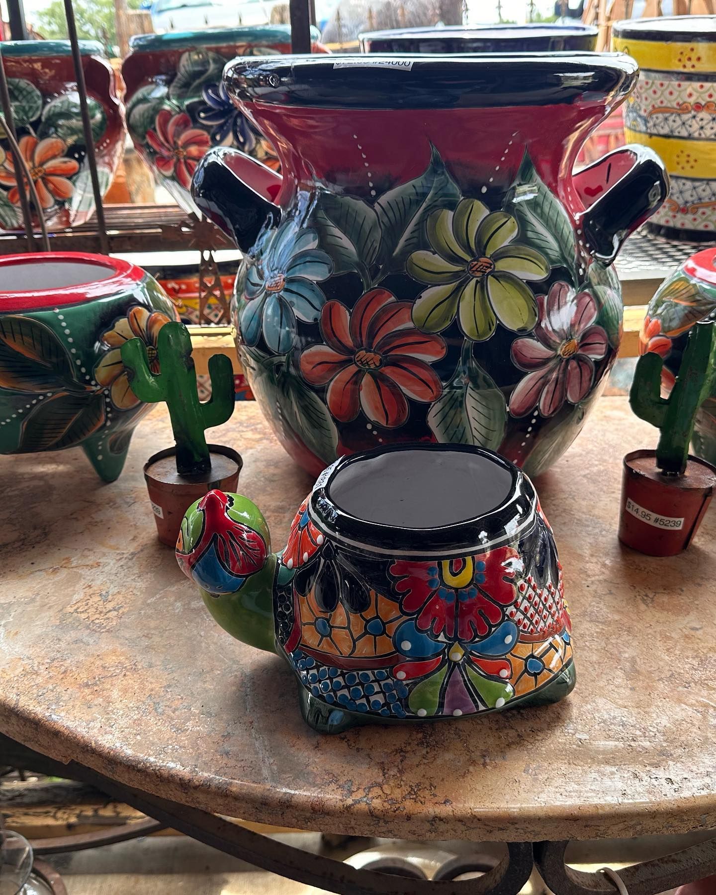 Colorful ceramic pots with floral designs and a turtle-shaped pot on a tabletop, likely in a shop.