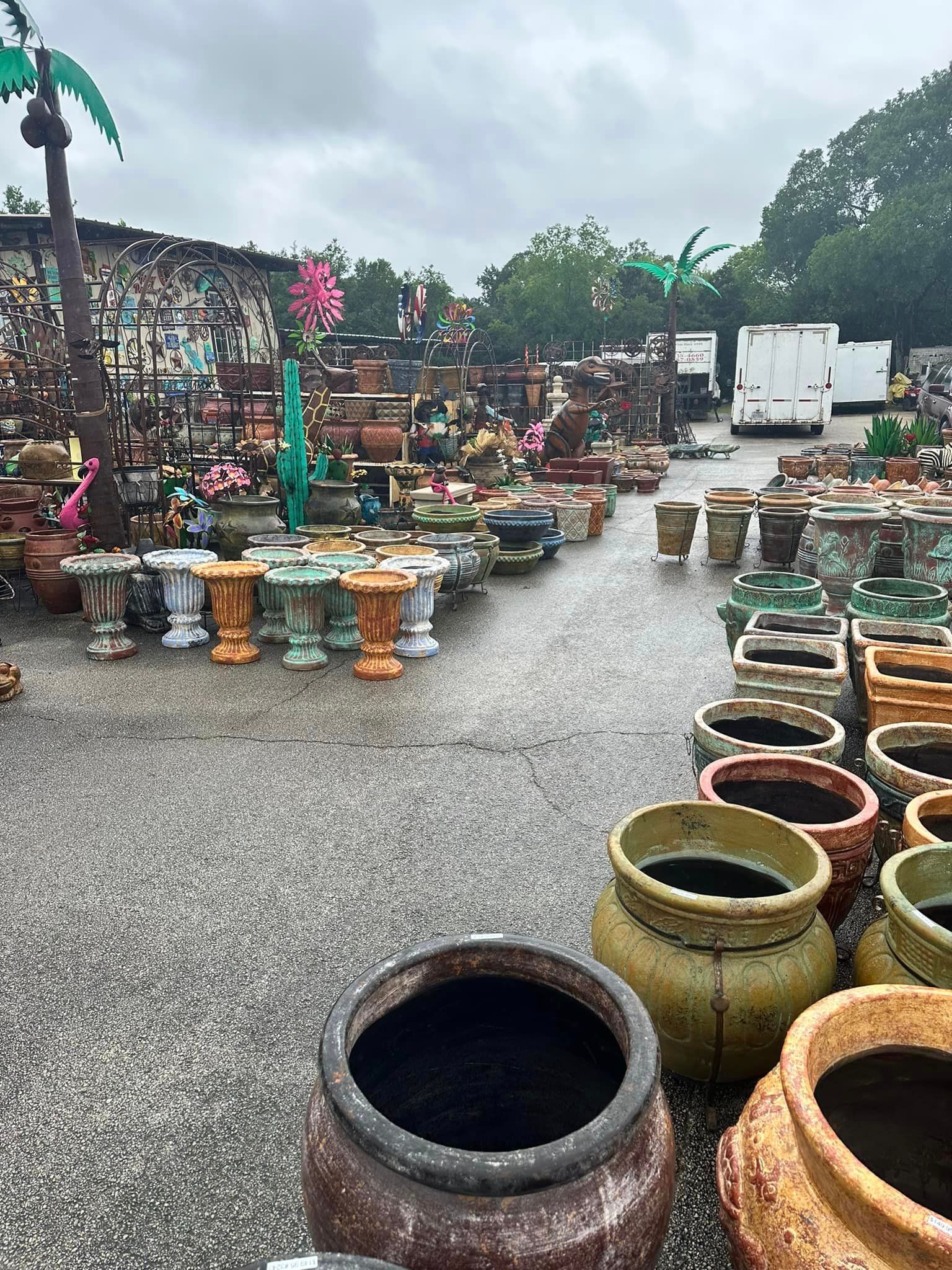 Outdoor shot of a garden center with rows of various ceramic and concrete pots, in various colors, on a rainy day.