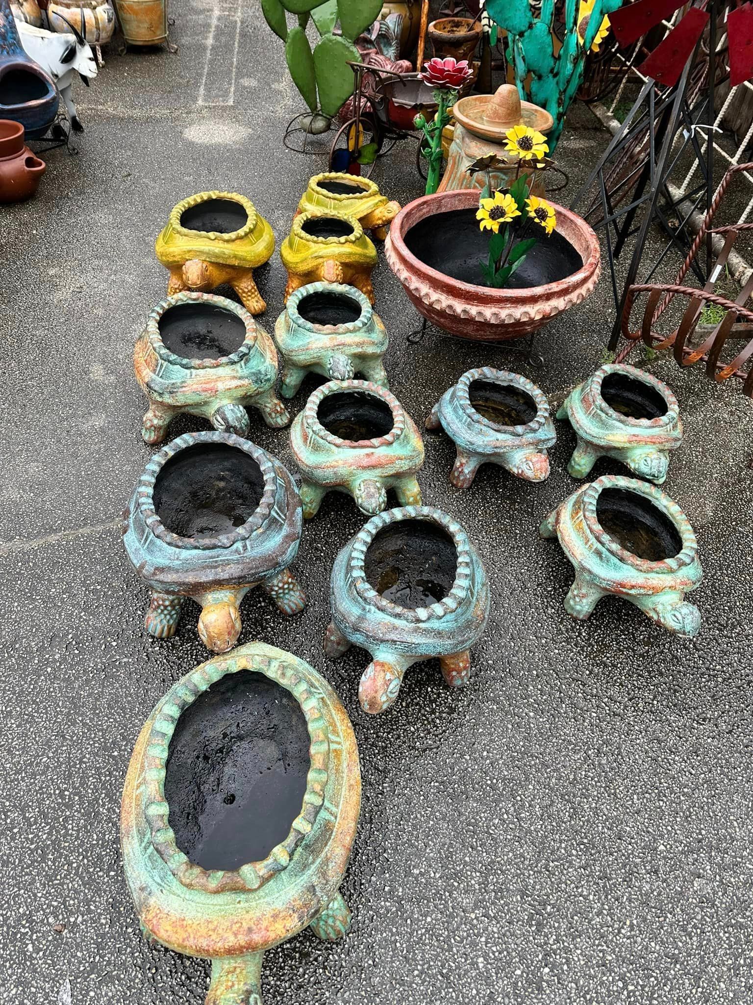 A collection of colorful turtle-shaped planters displayed on an outdoor surface. Some planters are empty, while one contains sunflowers.