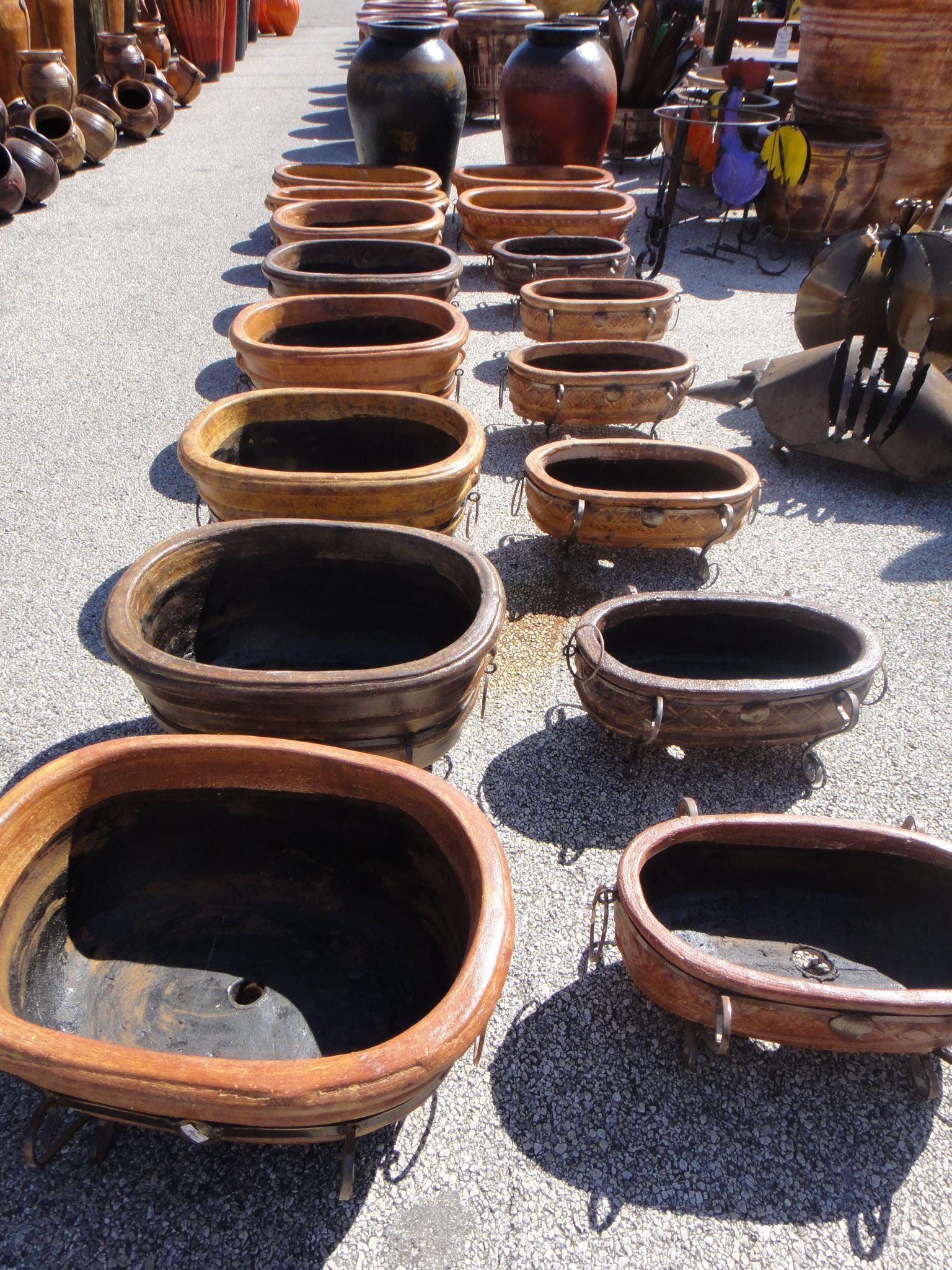 Rows of various-sized, open-topped, brown ceramic pots displayed outdoors for sale.