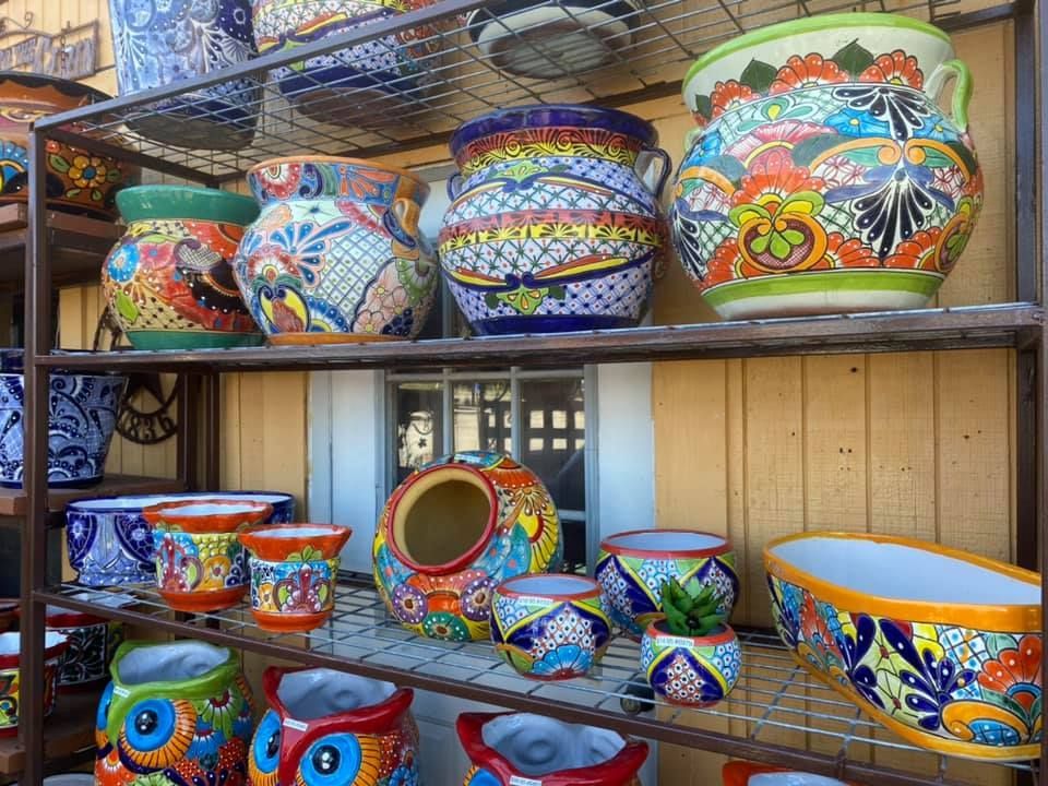 Shelves displaying colorful, hand-painted Talavera pottery in front of a yellow building. Various sizes and patterns, including owls and floral designs.