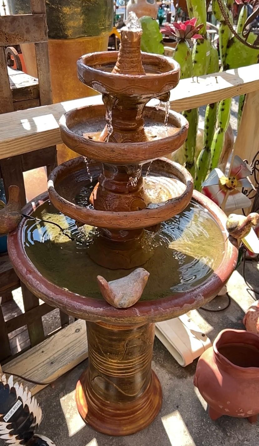 A tiered, brown water fountain with water flowing. A small bird statue sits on the base.