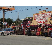 An old furniture store with a colorful, cluttered facade, a patriotic vehicle, and balloons, located in an outdoor setting.