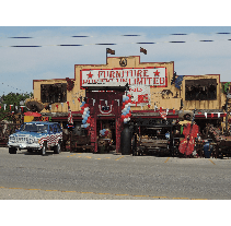 Exterior of Furniture Unlimited store with patriotic decorations, a flag-painted Jeep, and various displays on the road.