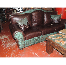 Brown leather sofa with teal accents and matching pillows in a room with a red floor and wood table.