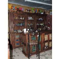 A rustic wooden bar with shelves displaying decorations and a bar stool in front. The bar is in a room with colorful signage.