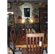 A rustic dining room with a wooden table and chairs, set with red dishes. A large mirror is mounted on the wall.