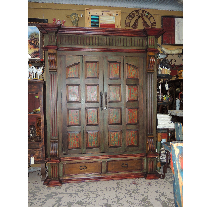 Large, ornately carved wooden cabinet with two doors and two drawers, in a room with other furniture.