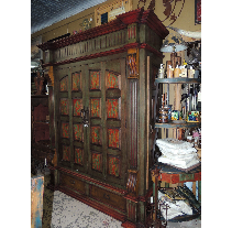 Large, ornate, wooden armoire with green, brown, and red paint. It is in a shop with other items on shelves and tables.