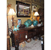 A dark wooden console table displays turquoise vases, a framed painting, and lamps.  The setting appears to be an antique shop.