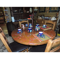 Round wooden dining table set with blue and floral teacups and saucers, surrounded by wooden chairs in a room setting.