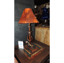 A rustic lamp with a copper lampshade sits on a wooden table with a colorful, patterned surface.