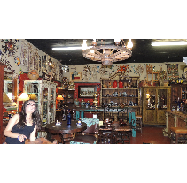 A woman smiles in a cluttered antique store with Southwestern style decor, including furniture, rugs, and a decorative ceiling fan.