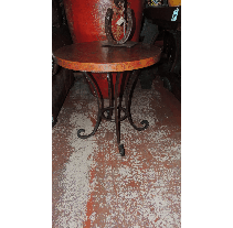 Round wooden table with wrought iron legs; horseshoe decoration on top. Set on a reddish-brown floor.