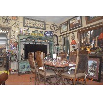 Dining room with a wooden table set for a meal, surrounded by ornate, carved chairs. The room has decorated walls with artwork and furniture.