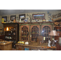 A rustic furniture store display.  Two ornate wooden cabinets hold items, with artwork and decorations displayed above.