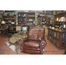 A brown leather recliner chair in a room filled with rustic furniture and decor, including shelves and a coffee table.