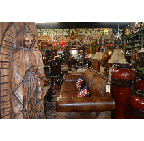 Inside a shop, a carved wooden statue of a robed figure stands left. A leather sofa with American flag pillows sits center.