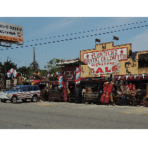 A furniture store with a SALE sign, an American flag-themed jeep, and red, white, and blue decorations under a blue sky.