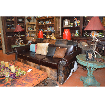 Living room with a brown leather couch, rustic coffee table, and side table with red lamps and decorative items.