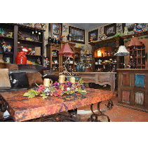 Interior of a shop with rustic furniture and decor, including a copper-topped table, shelves, and various items for sale.