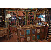 Wooden furniture display: A central island with colorful panels is surrounded by cabinets and tables in a rustic, southwestern style.
