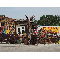 A cluttered roadside shop with rusty metal sculptures in front and a sign reading Western & Rustic Antiques.