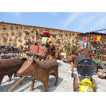 Metal yard art featuring a cowboy in a wagon pulled by brown metal oxen; setting is a yard on a sunny day.