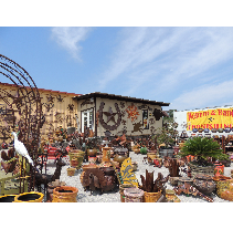 A shop displaying various outdoor decor, including pots, statues, and a western-themed building against a blue sky.