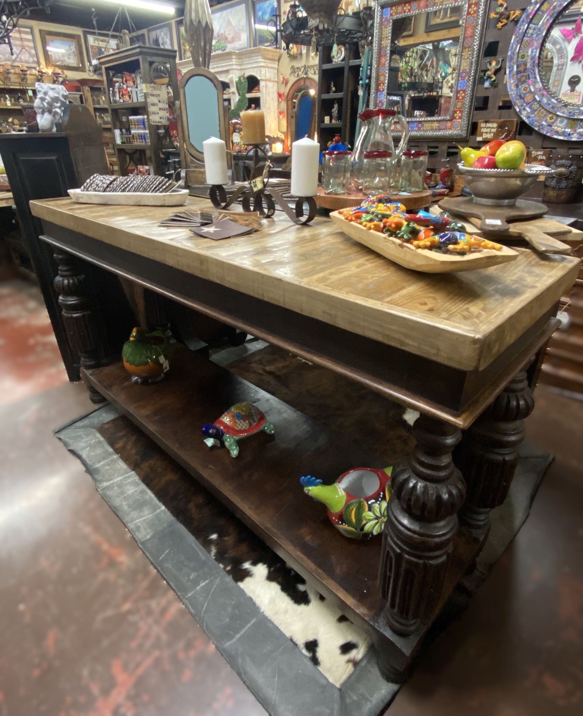 Large wooden table with decorative legs, various items on top and lower shelf, in a store setting.