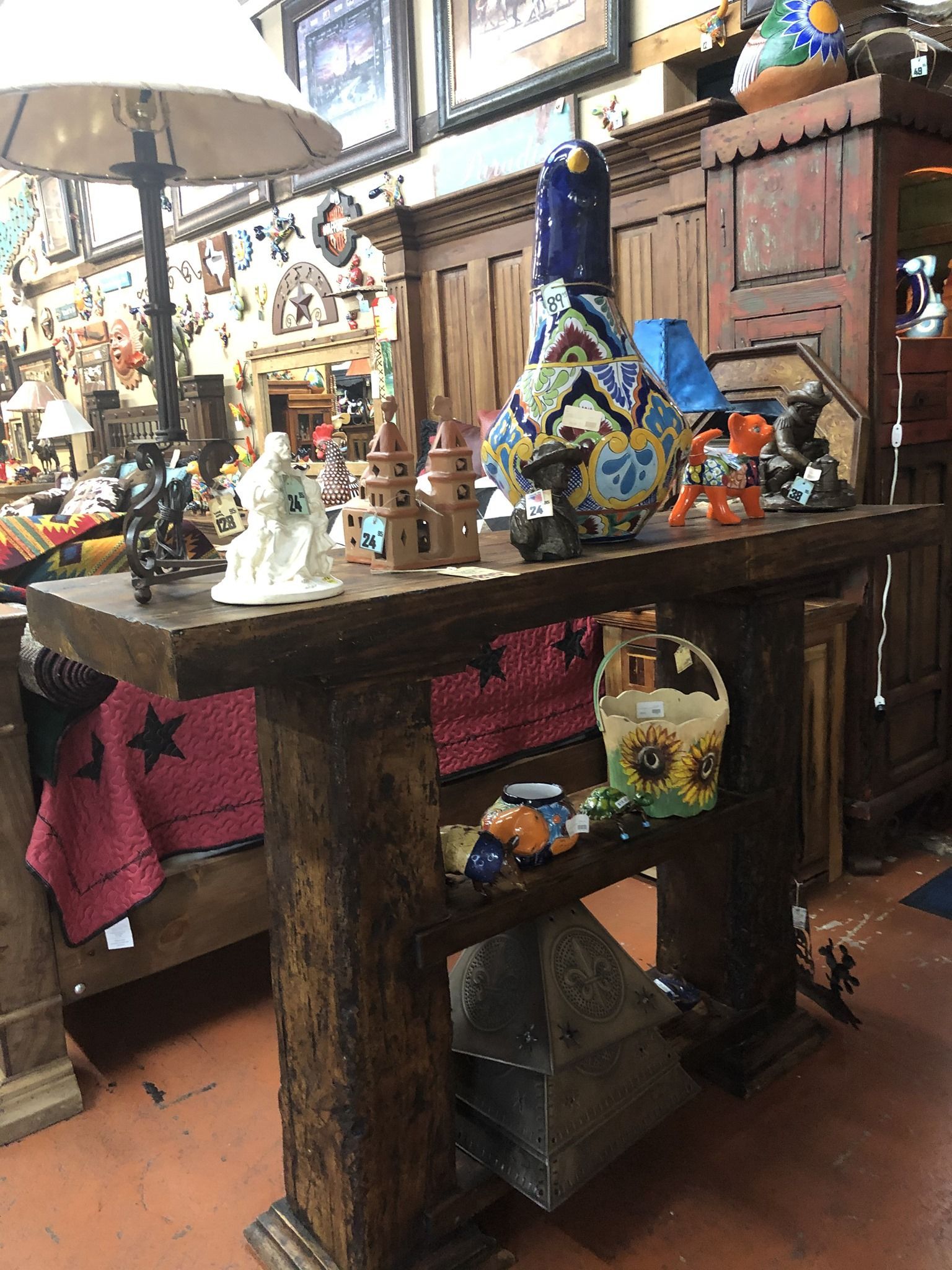 Wooden table displaying various decorative items in a cluttered shop setting. Items include pottery, lamps, and figurines.