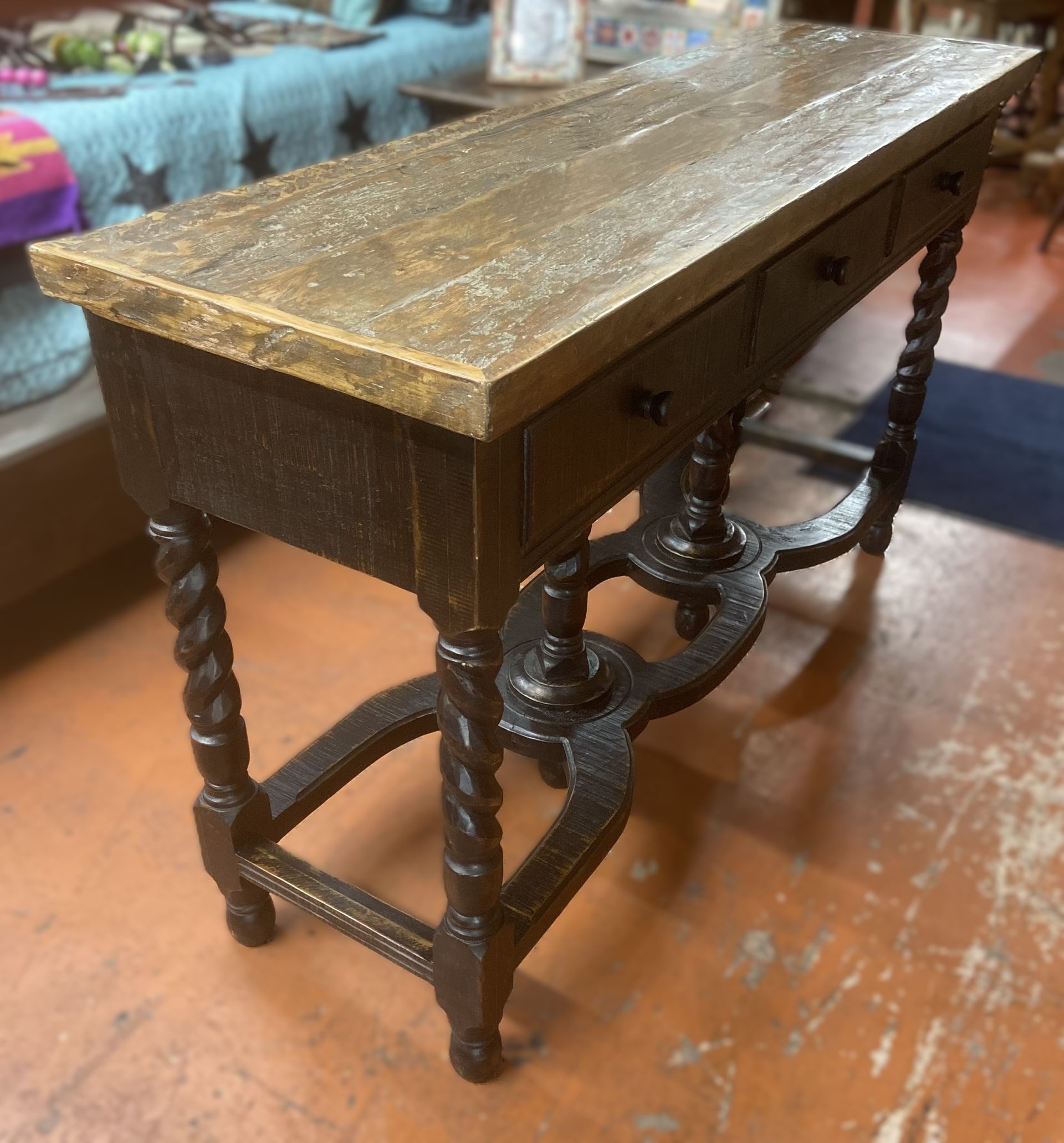 Antique wooden console table with a dark brown frame, three small drawers, and a light brown tabletop. The legs are twisted with a decorative crossbar.