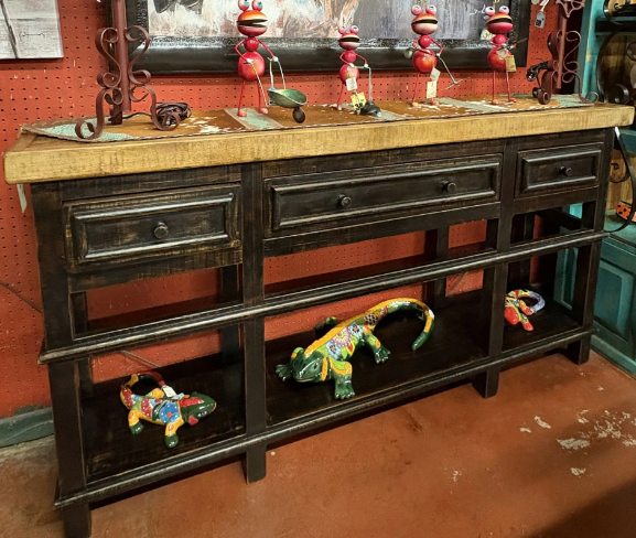 A rustic black wooden console table with drawers and a shelf, decorated with colorful lizard sculptures and whimsical frog figurines.