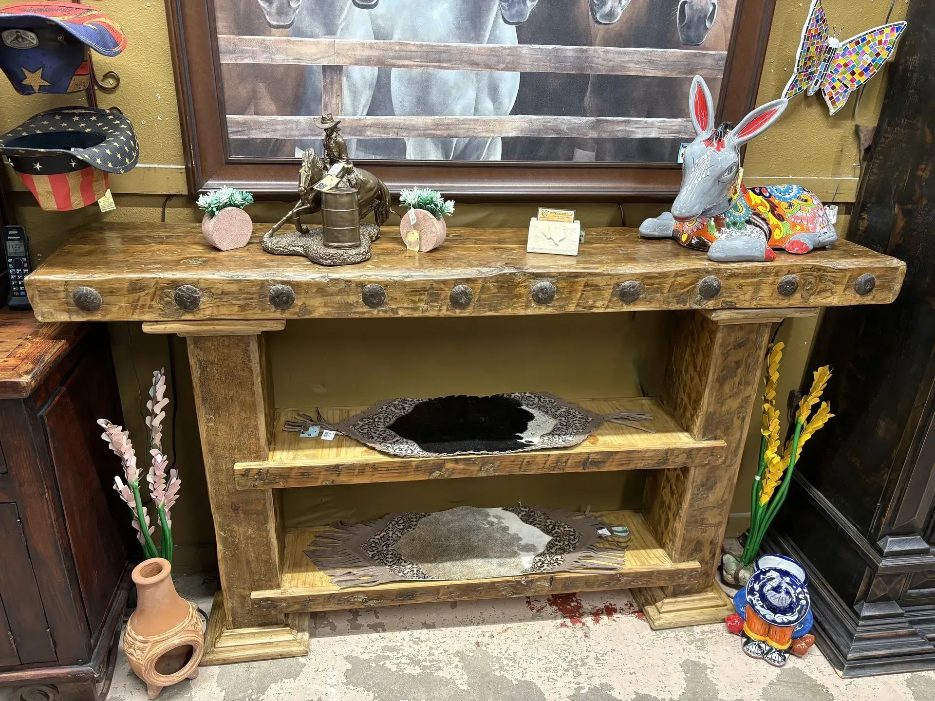 Wooden console table with objects on top and shelves, including a decorative bunny, mirror, and vases.