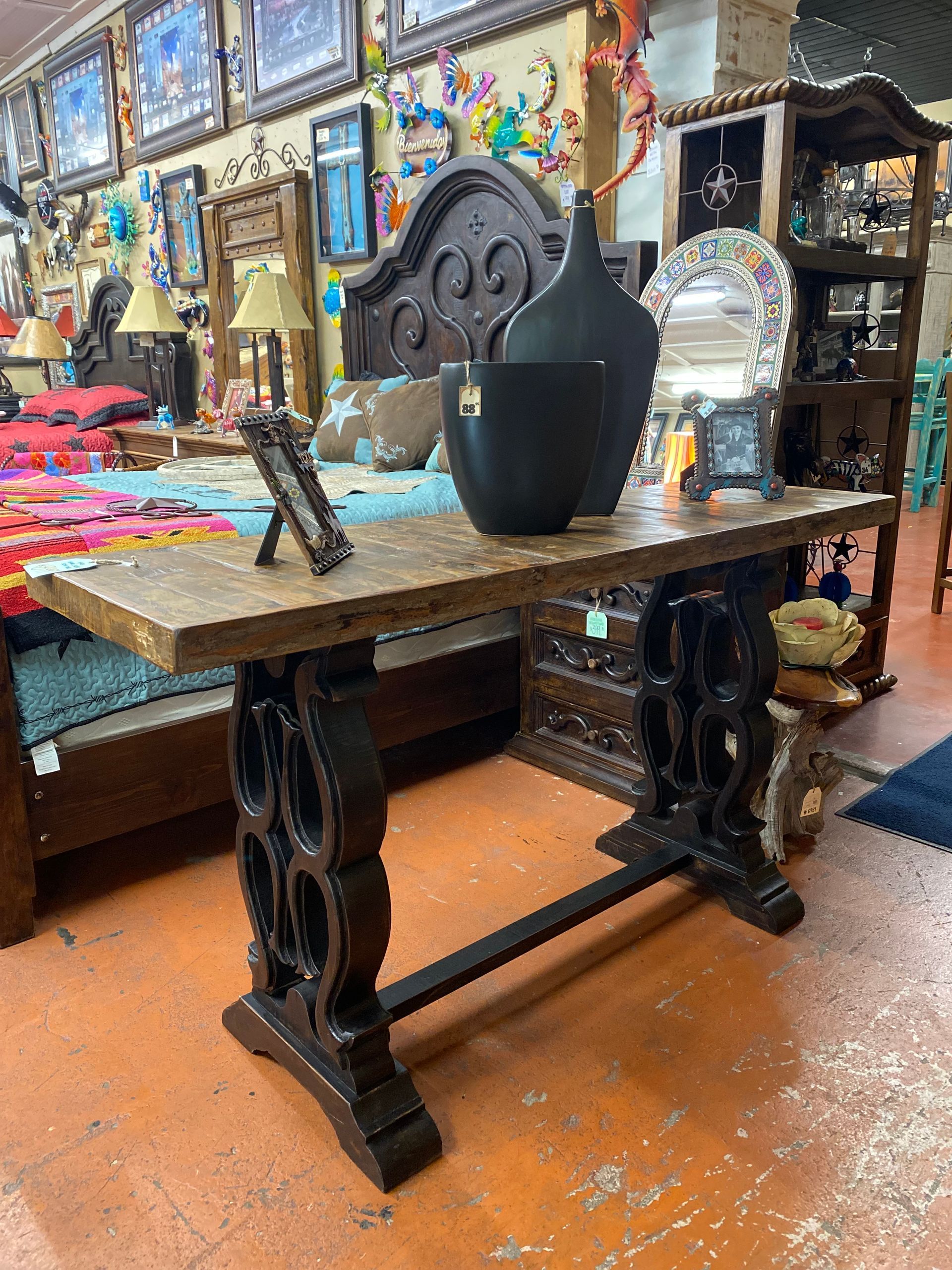 A rustic brown wooden console table with decorative legs, holding black vases and a picture frame, inside a shop.