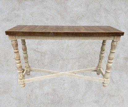 Wooden console table with turned legs and an X-shaped brace, featuring a light cream base and a brown tabletop, set against a textured background.