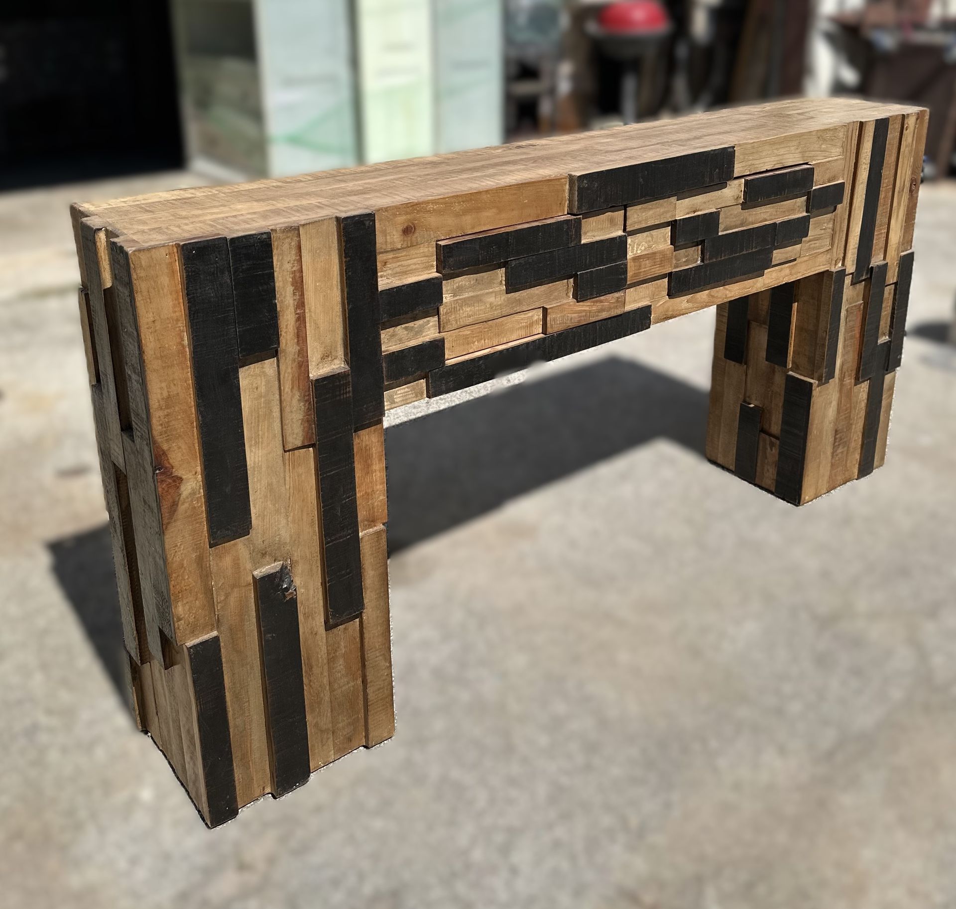 Wooden console table with a mosaic design of natural and black wood blocks. It has a rectangular top and two rectangular legs.