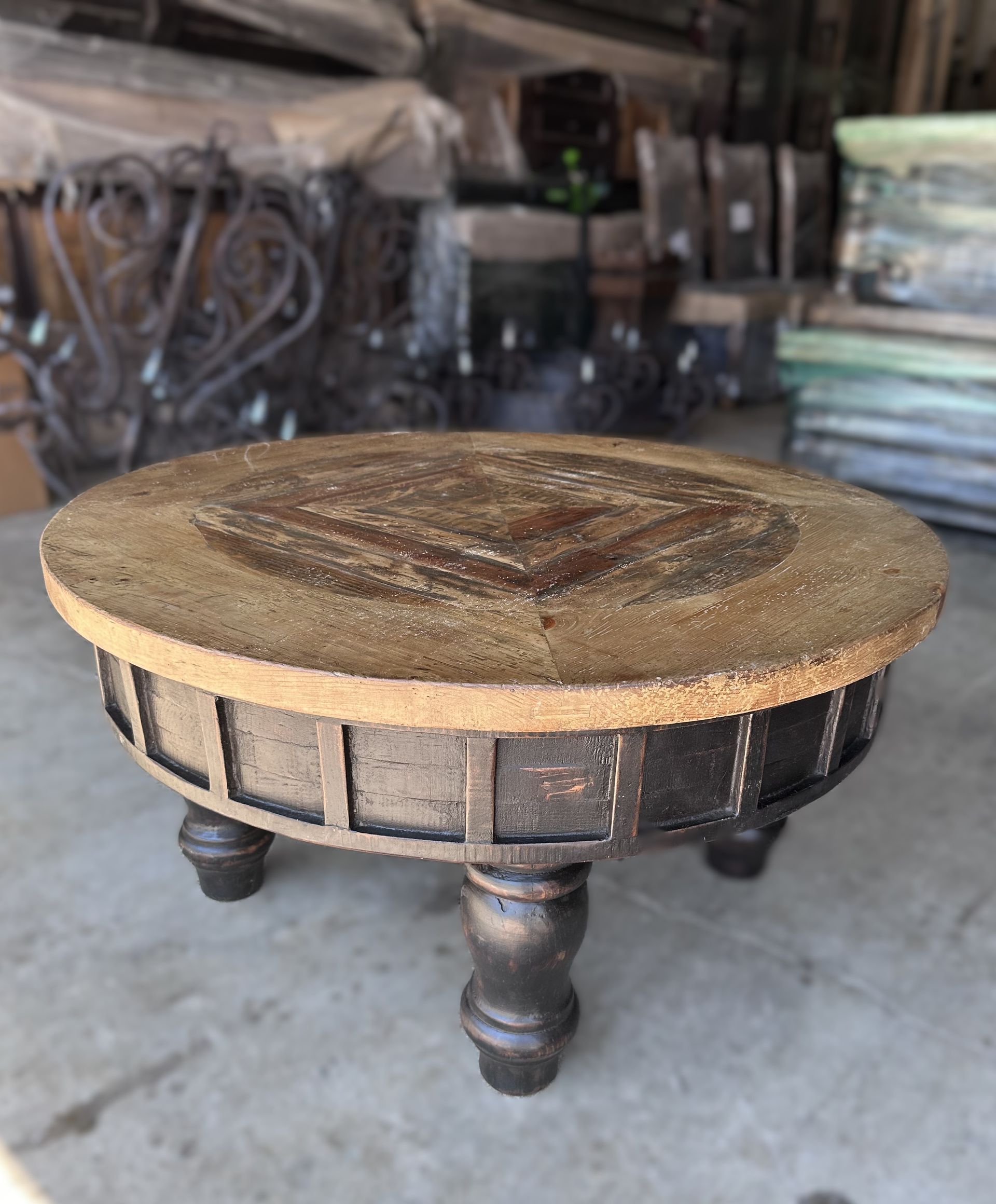 Round, dark brown wooden table with short legs and a textured top, set in a storage or warehouse area.