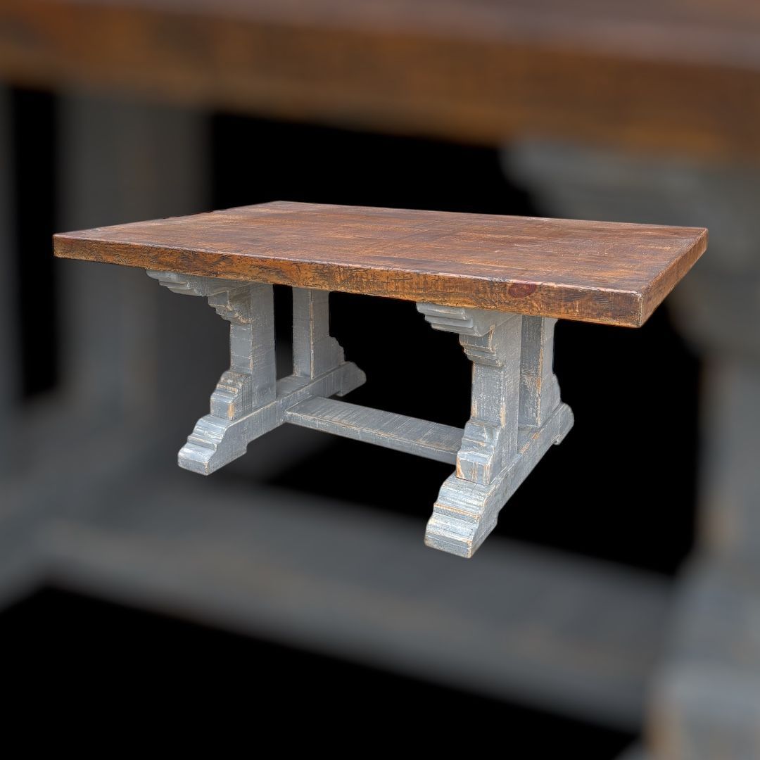 A rustic wooden table with a brown top and ornate gray legs, set against a blurred background.