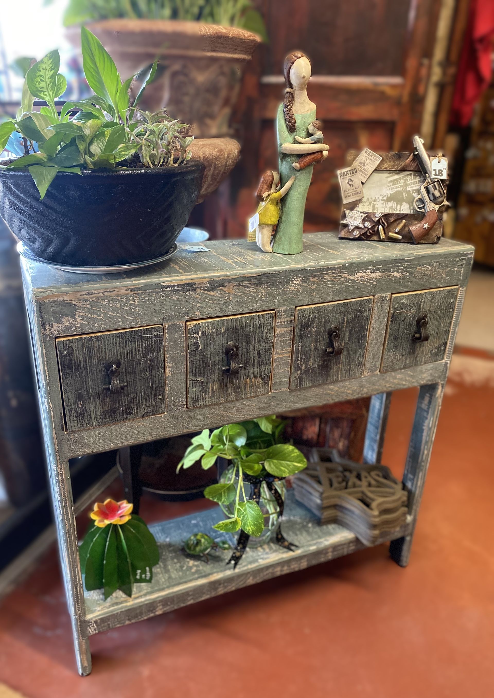 A rustic, weathered gray console table with potted plants, figurines, and decor, indoors.