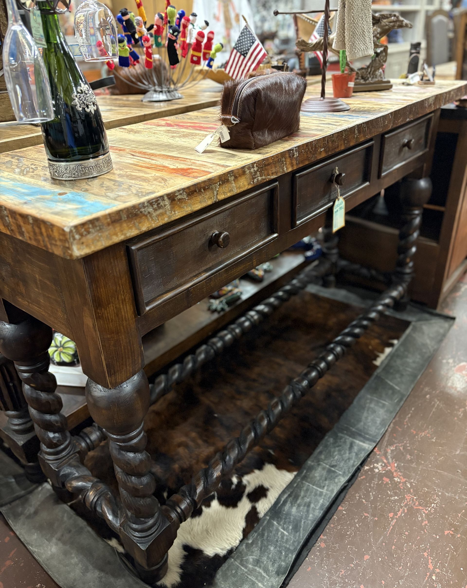 Wooden console table with drawers, a cowhide rug, and decorative items in a retail setting.