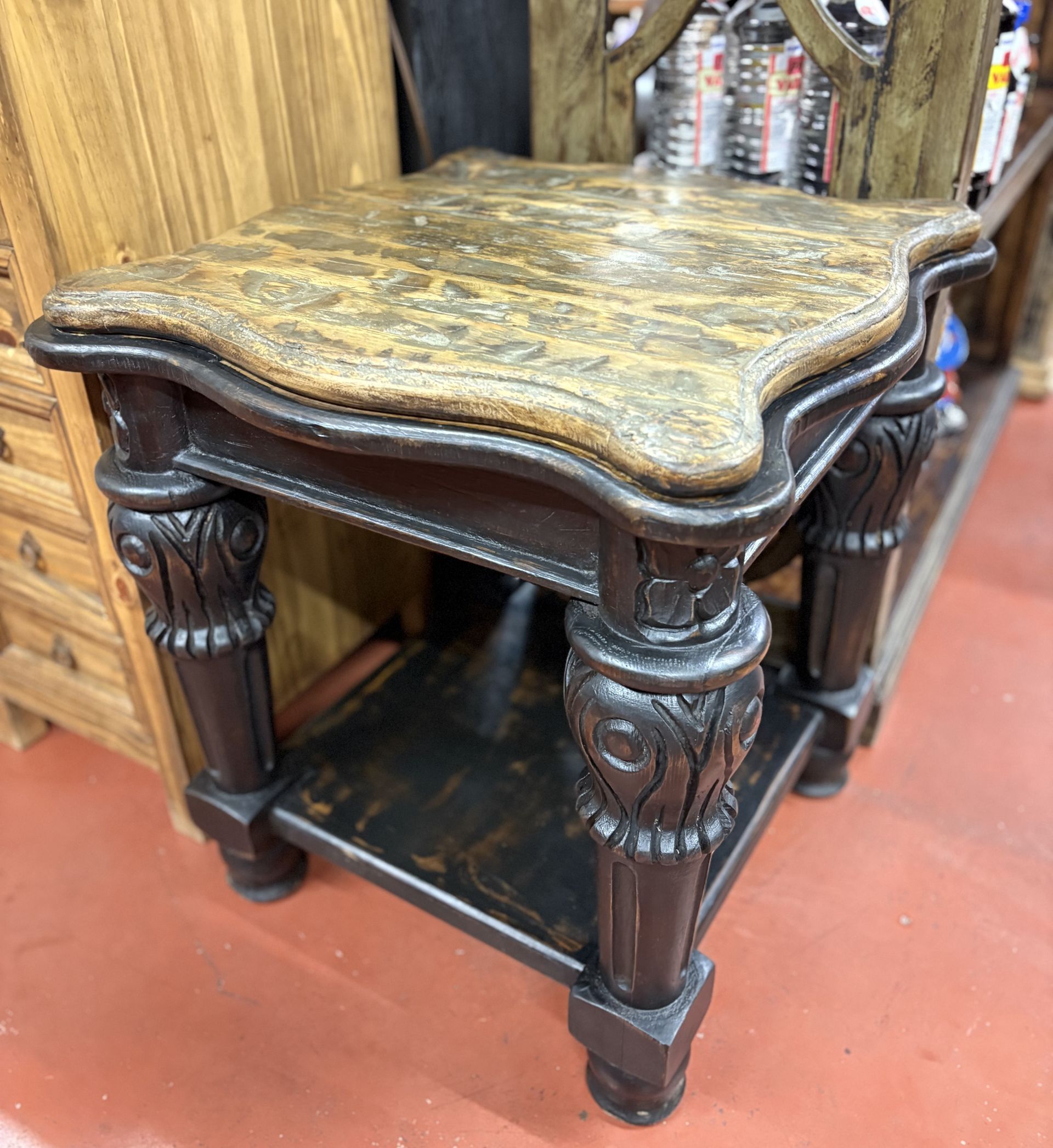 A small, ornate side table with a patterned top and dark, carved legs. It sits on a lower shelf.