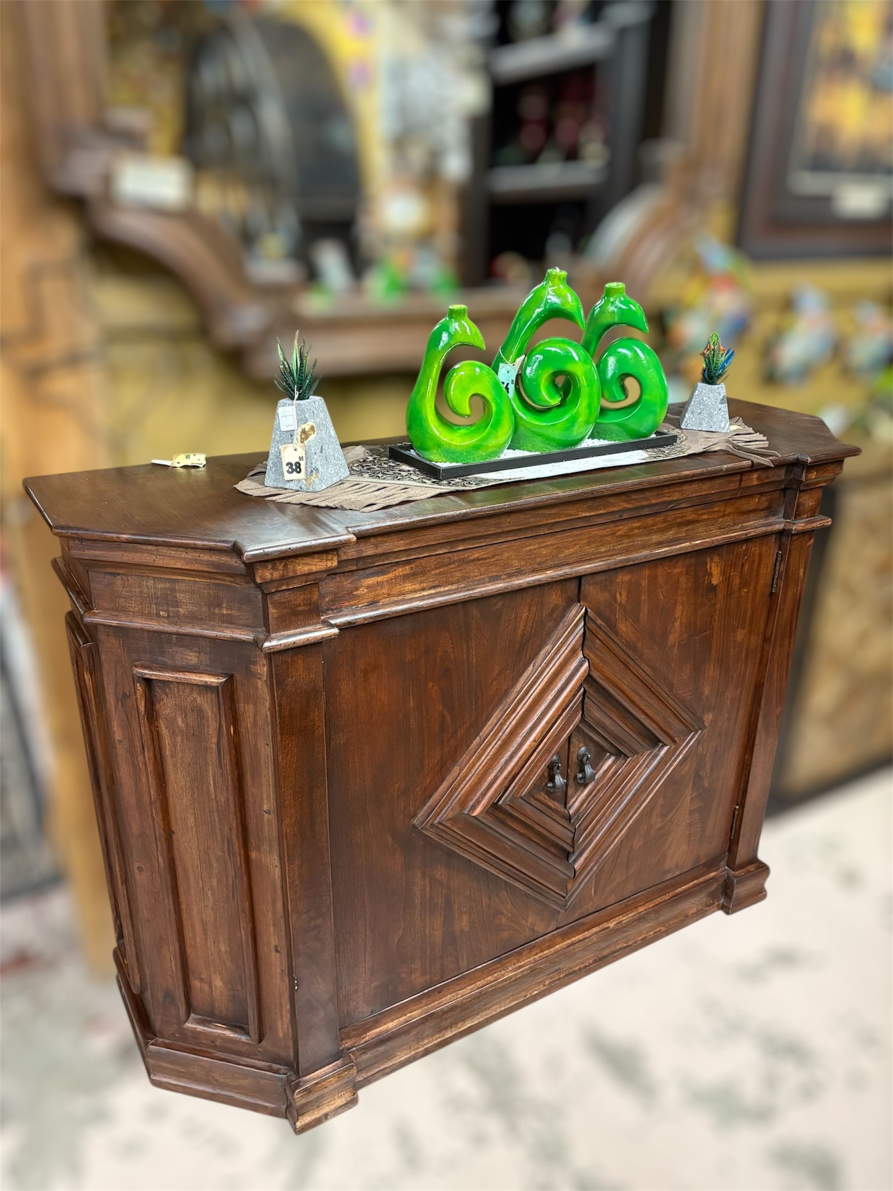 A dark wooden bar with decorative diamond detail, topped with green sculpted art pieces and small structures.