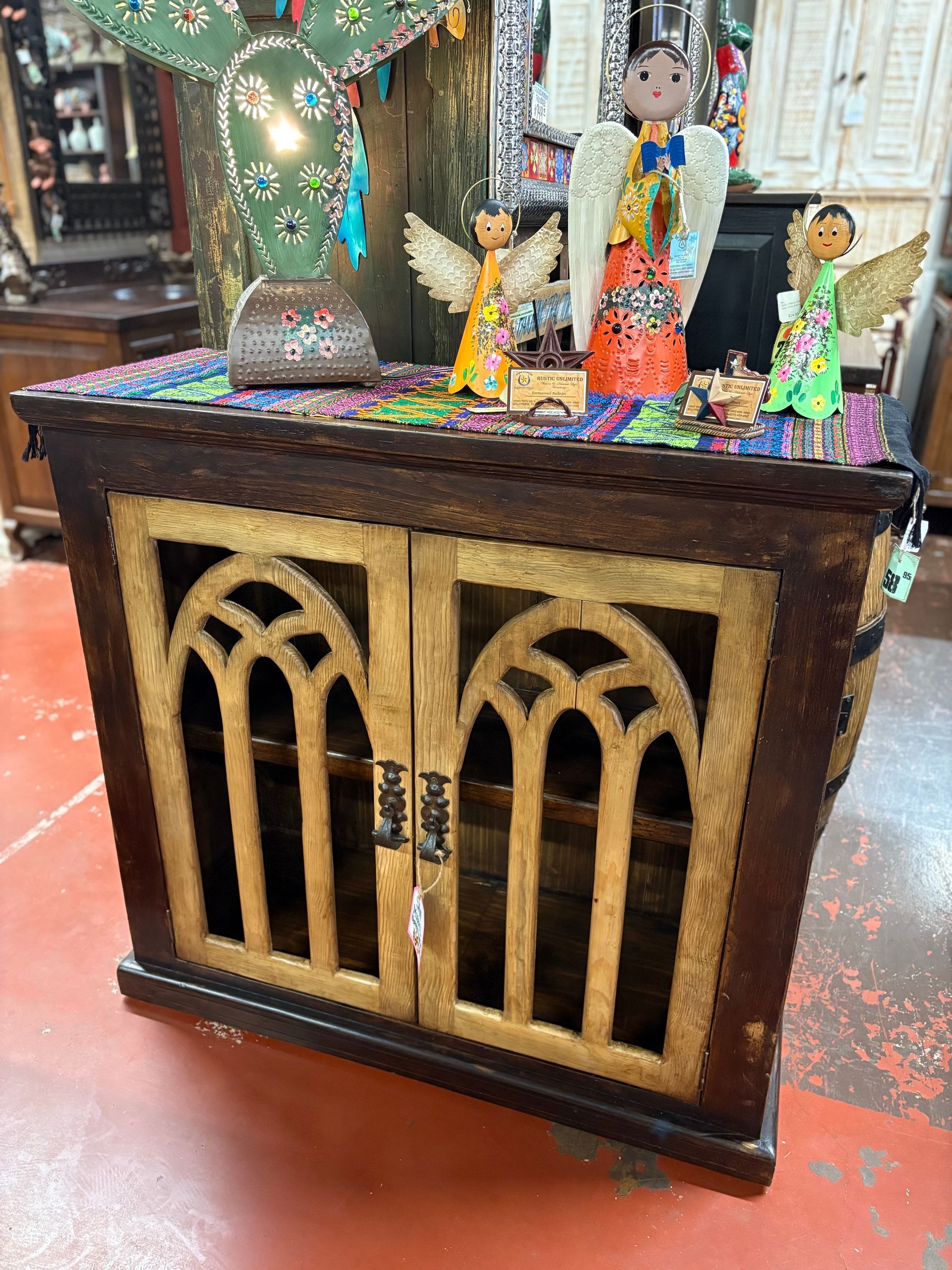 A wooden cabinet with arched gold doors, topped with colorful decorations and angel figurines.
